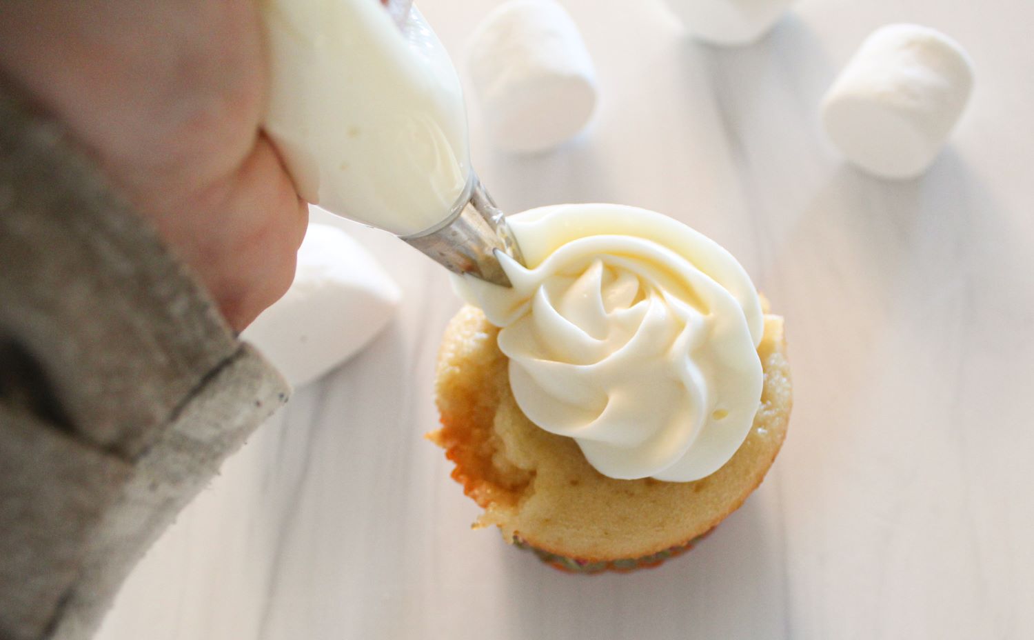 piping swirl of marshmallow icing onto cupcakes